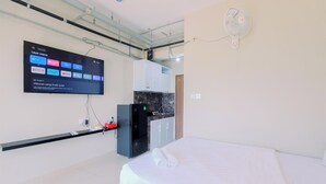 A hotel room with a bed, a TV mounted on the wall displaying streaming services, a small kitchenette, and a ceiling fan. - Homey And Restful Studio Royal Sentul Park Apartment (Bogor)