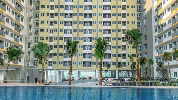 A high-rise residential building with a swimming pool in the foreground. - Cozy And Restful Studio Lrt City Sentul - Royal Sentul Park Apartment (Bogor)