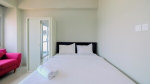 A hotel room with a bed, a red chair, and a door leading to a balcony. - Cozy And Restful Studio Lrt City Sentul - Royal Sentul Park Apartment (Bogor)