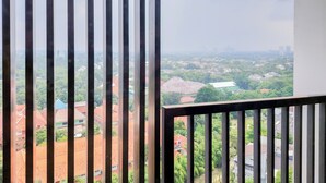 A balcony with vertical blinds, offering a view of a cityscape with buildings and greenery. - Comfy And Modern Studio Room The Ayoma Apartment (South Tangerang)