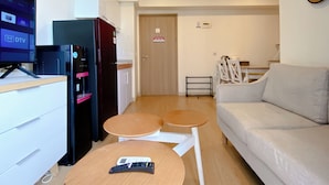 A modern living room with a sofa, a TV, a refrigerator, and a small table with a remote control. - Clean And Homey 2Br At Meikarta Apartment (Cikarang)