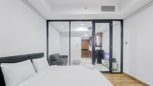 Quarto de hotel com cama, cabeceira preta, colchão branco, sofá preto, mesa redonda pequena e uma televisão.