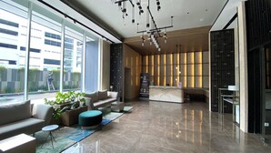 Um lobby moderno com balcão de recepção, área de estar e grandes janelas com vista para o exterior.