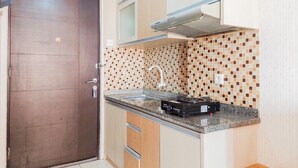 Una cocina compacta con puerta de madera oscura, salpicadero de azulejos, un lavamanos de acero inoxidable y una campana extractora empotrada.