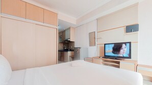 Habitación de hotel con cama, televisión, escritorio y kitchenette.
