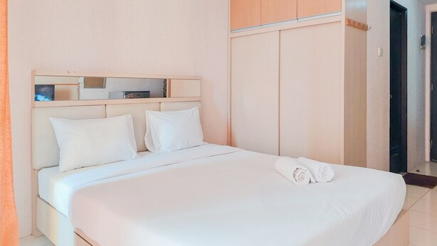 Una cama bien hecha con sábanas y almohadas blancas, un cabecero de madera y un armario con espejo.