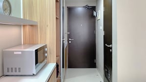 A kitchen with a microwave, wooden cabinets, and a door leading to another room. - Simply Look Studio At Mustika Golf Residence (No Kitchen) Apartment (Cikarang)
