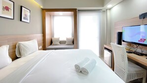 A hotel room with a bed, a desk with a computer, a television, and a window with curtains. - Simply Look Studio At Mustika Golf Residence (No Kitchen) Apartment (Cikarang)