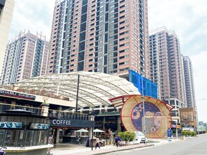 Eine moderne Stadtstraße mit Hochhäusern, einer überdachten Außenbereich-Sitzgelegenheit und verschiedenen Geschäften, darunter ein Café.