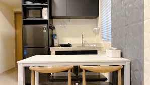 Eine kompakte Küche mit Kühlschrank, Mikrowelle und Spüle. Ein kleiner Esstisch mit zwei Stühlen steht daneben.