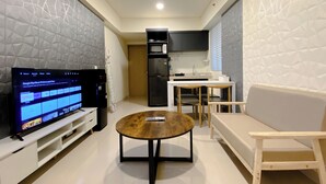 Ein modernes Wohnzimmer mit Fernseher, einem runden Holztisch, einer Couch und einer Küchenzeile mit Kühlschrank und Mikrowelle.