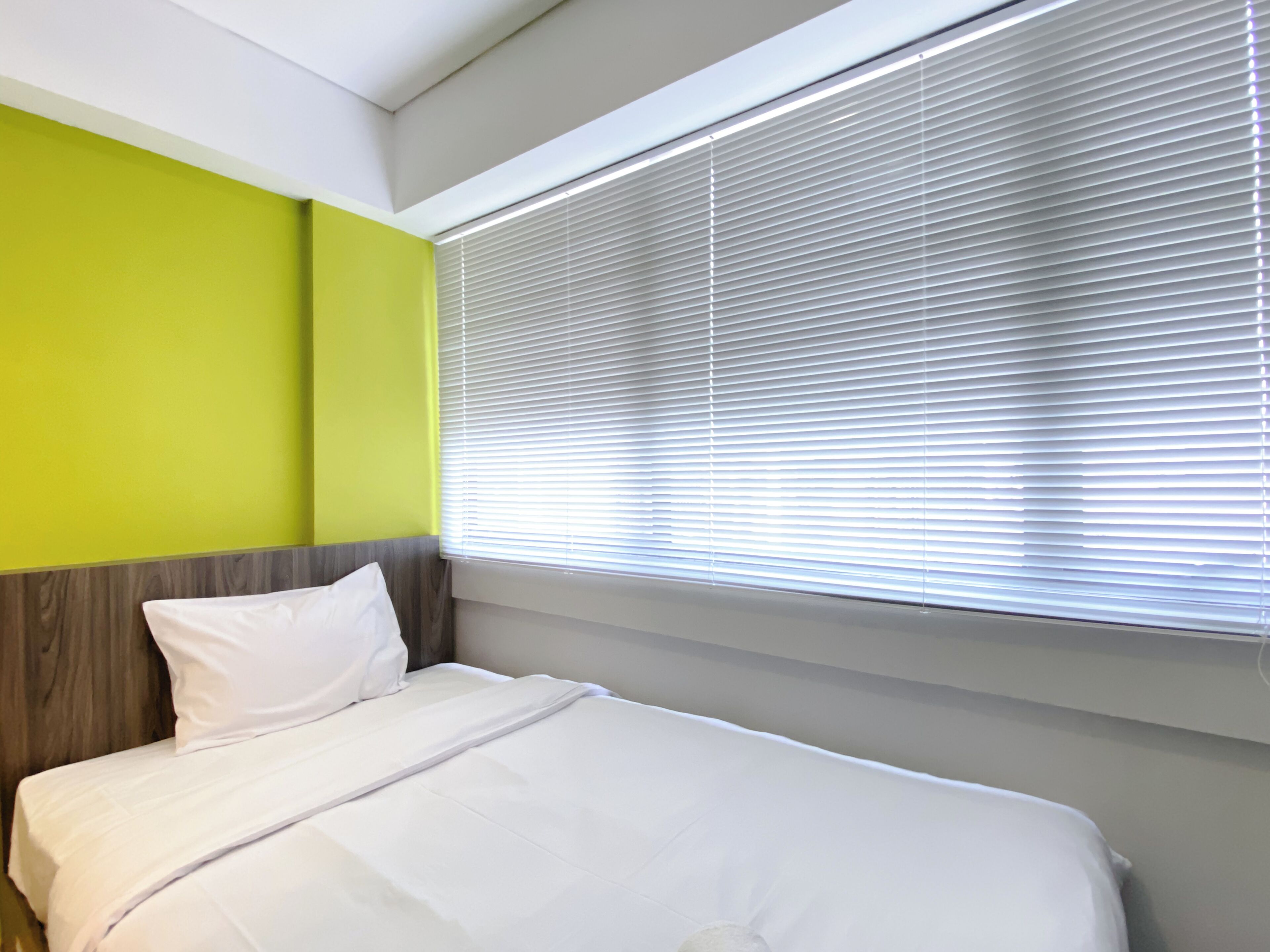 A hotel room with a bed, a window with blinds, and a green wall.