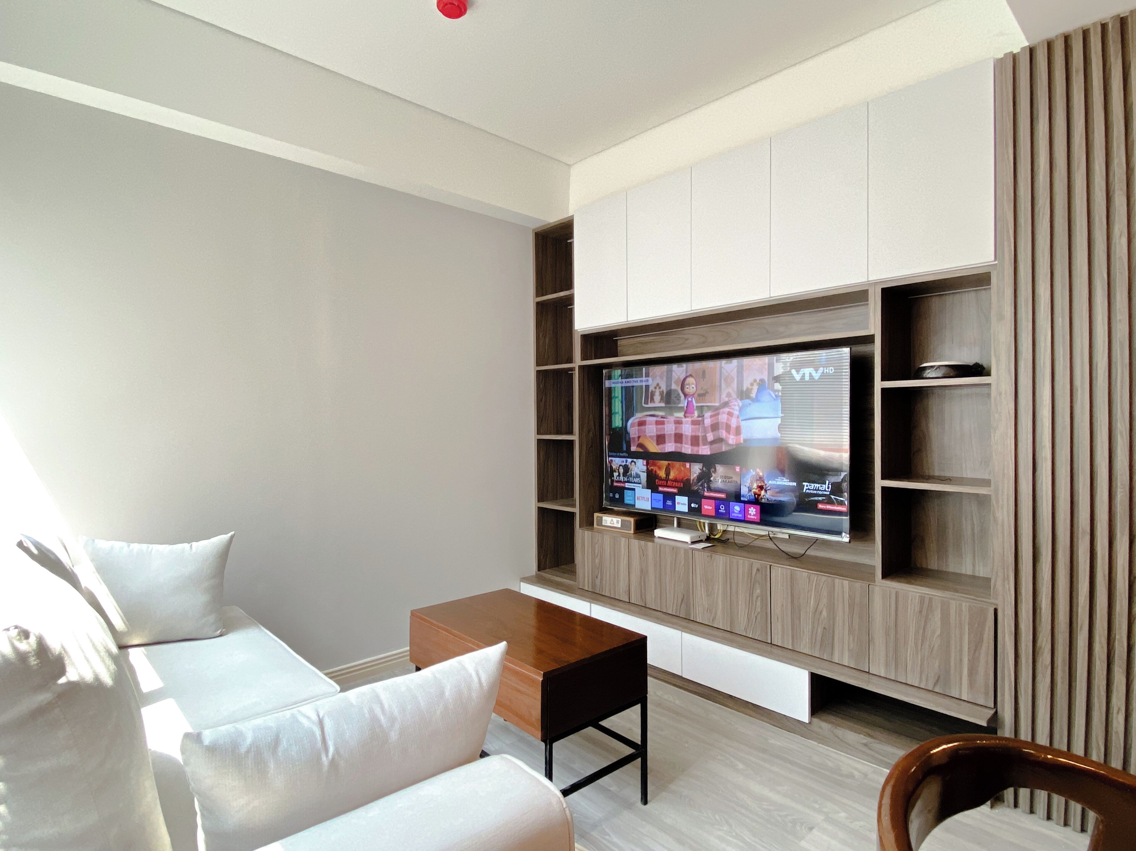 Un salon moderne avec un téléviseur à écran plat fixé à un mur en bois, un canapé blanc, une table basse en bois et des étagères intégrées.