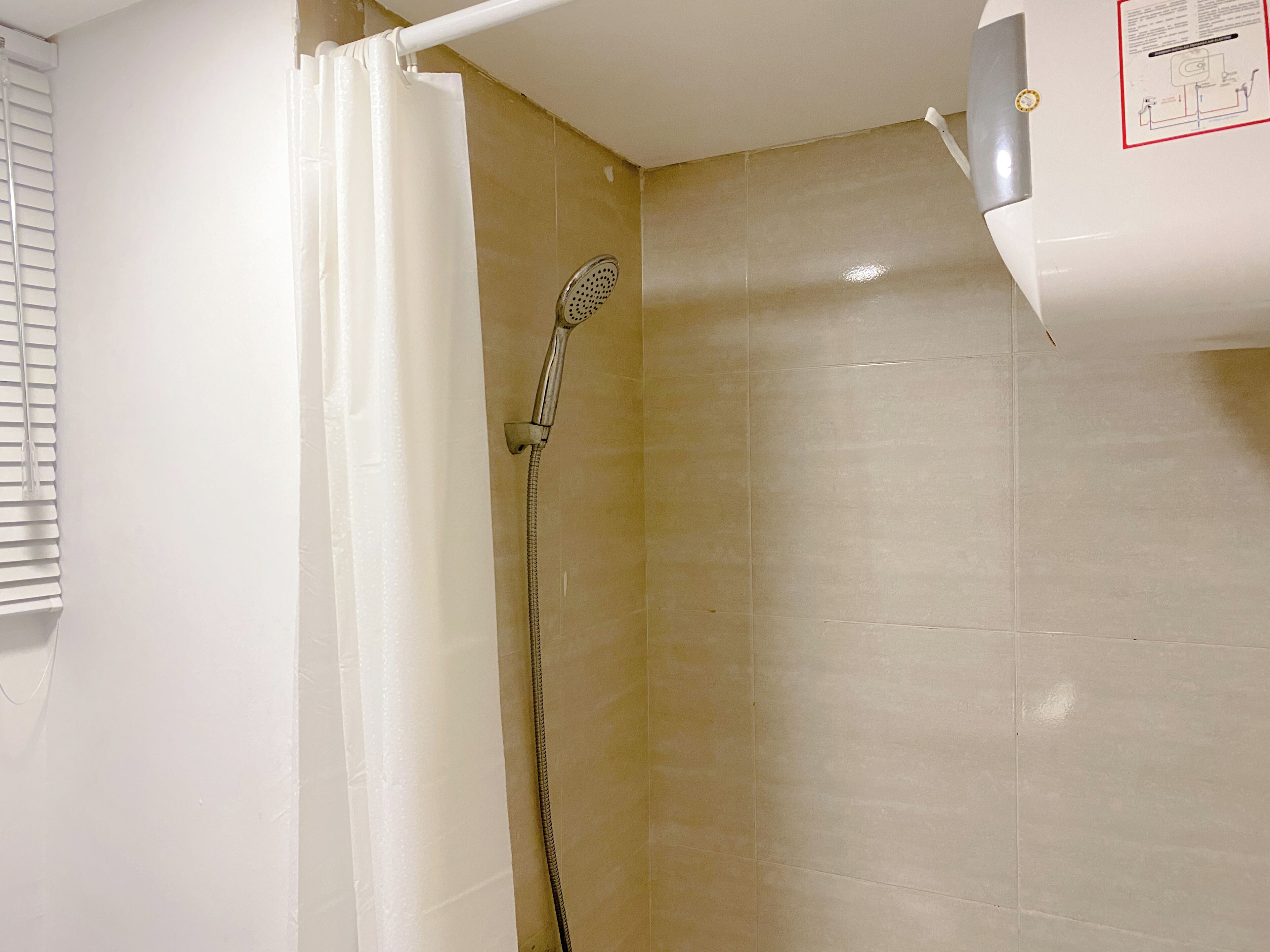 A shower with a handheld showerhead, a white curtain, and beige tiled walls.