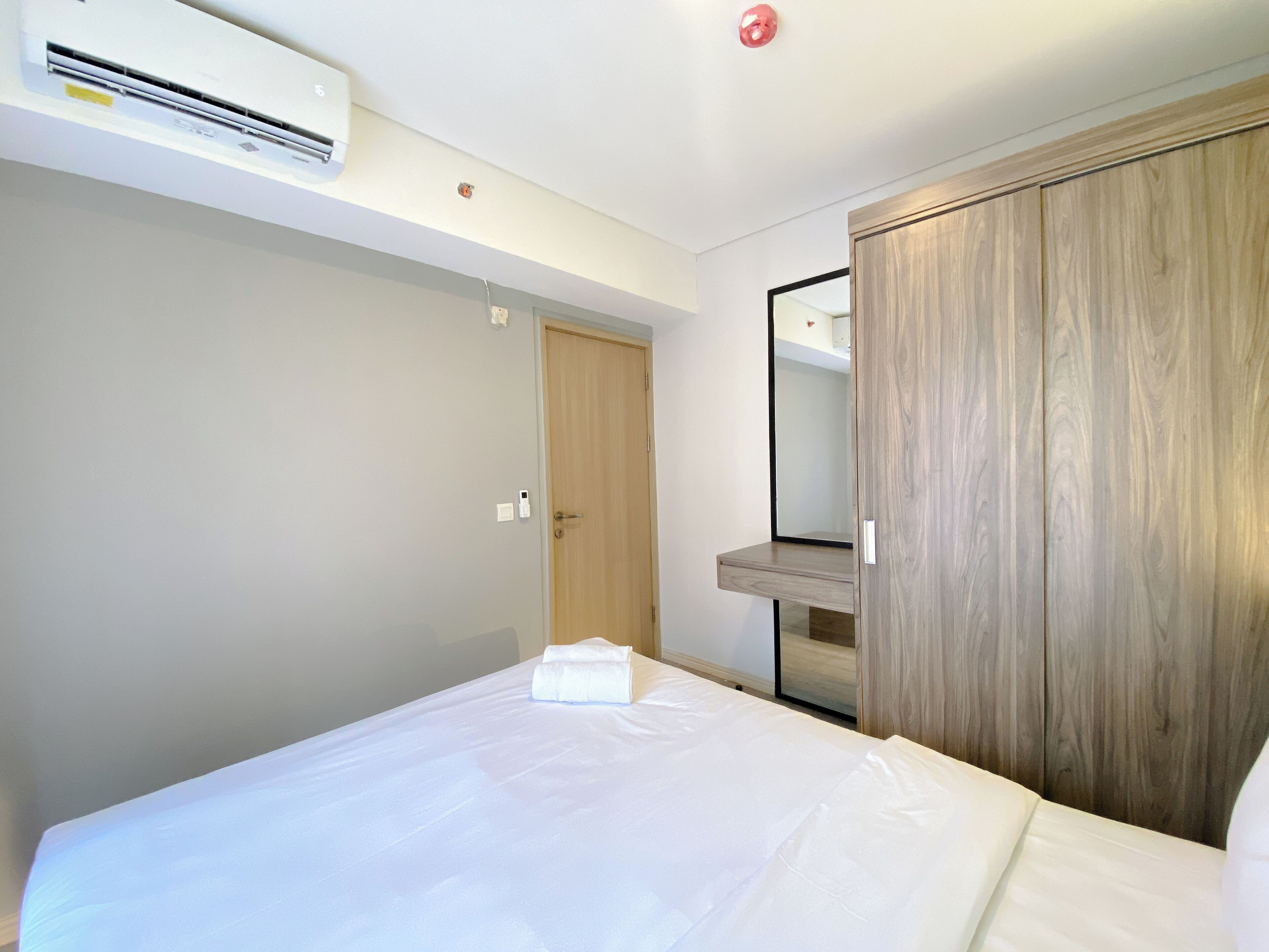 A hotel room with a bed, a wardrobe, a mirror, and an air conditioning unit.