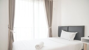 A neatly made bed with a rolled towel, a dark headboard, and a white bedside table. - Nice And Cozy Studio At Sky House Bsd Apartment (Pagedangan)