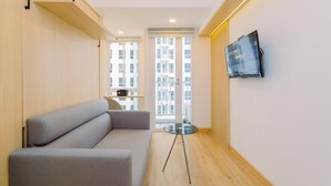 A modern living room with a grey sofa, a small glass table, and a mounted TV on the wall. - Simply Look And Cozy Studio Tokyo Riverside Pik 2 Apartment (Teluknaga)