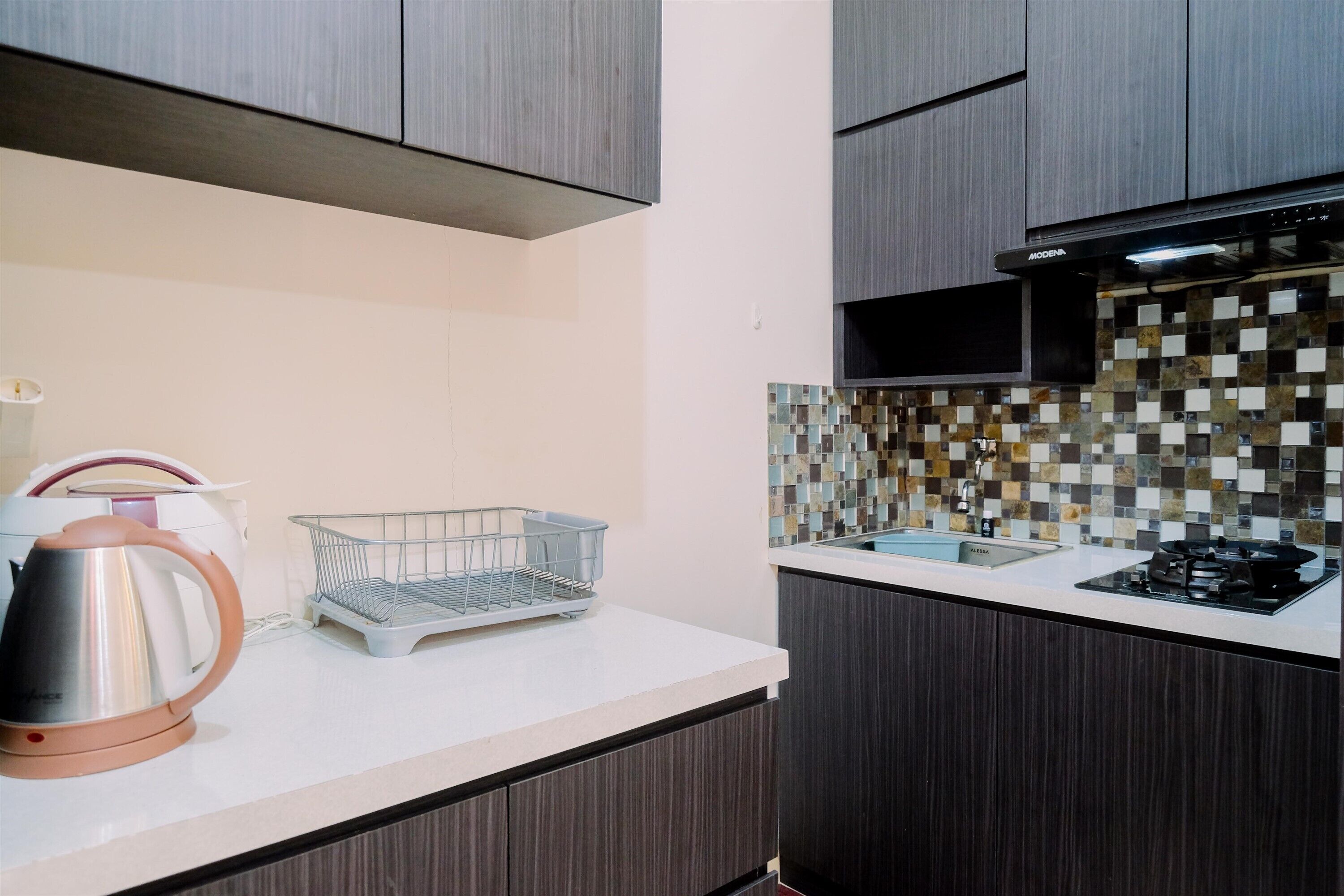 A modern kitchen with dark wooden cabinets, a white countertop, a tiled backsplash, and a stainless steel kettle.