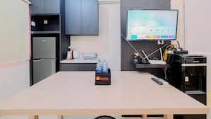 Ein modernes Zimmer mit einem wandmontierten Flachbildfernseher, einem Kühlschrank, einem Wasserspender und einem Reiseköfferchen auf dem Tisch.