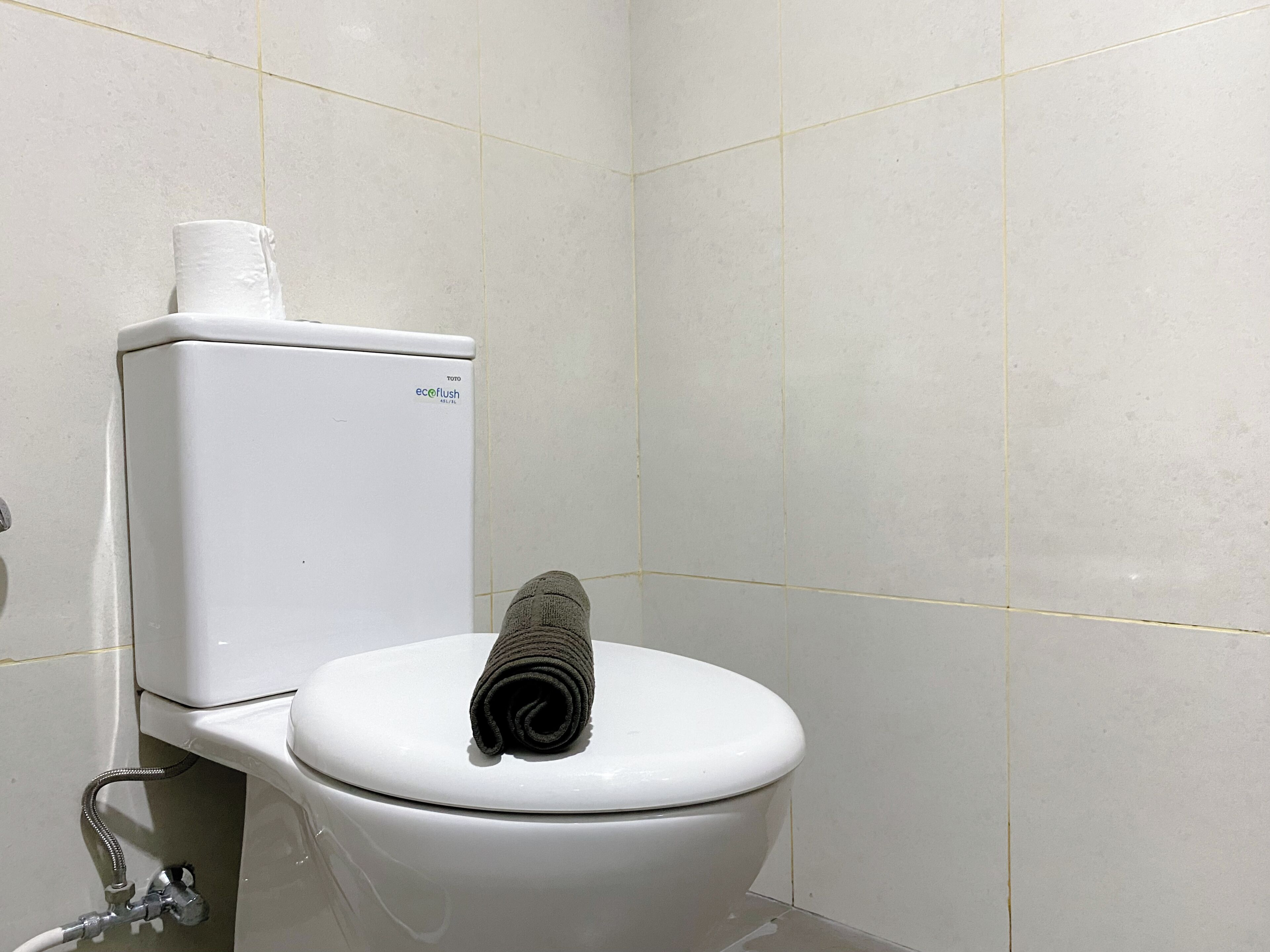 A white toilet with a towel on the lid, a toilet paper holder, and a visible water pipe.