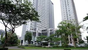 A modern building with a glass facade, surrounded by greenery and adjacent to taller residential buildings. - Best Price And Homey 1Br At Tamansari Prospero Apartment (Sidoarjo)