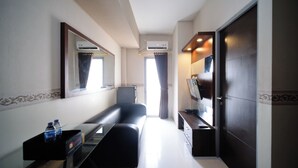 A hotel room with a bed, a bedside table with a water bottle, a mirror, an air conditioning unit, and a door. - Best Price And Homey 1Br At Tamansari Prospero Apartment (Sidoarjo)