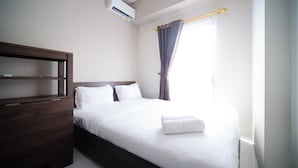 A neatly made bed with white linens and a folded towel, a wooden headboard, and a window with curtains. - Best Price And Homey 1Br At Tamansari Prospero Apartment (Sidoarjo)
