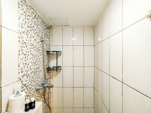 Une salle de bain avec une douche, des murs carrelés, un porte-rouleau de papier toilette et deux flacons de produits de toilette.