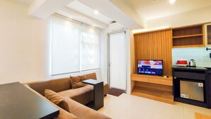 A modern living room with a sofa and a dining table, a kitchen with a TV, and a large window. - Spacious Classic Studio At Jarrdin Cihampelas Apartment (Bandung)