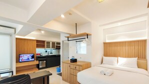 A modern hotel room with a bed, a desk, a TV, and a kitchen area. - Spacious Classic Studio At Jarrdin Cihampelas Apartment (Bandung)