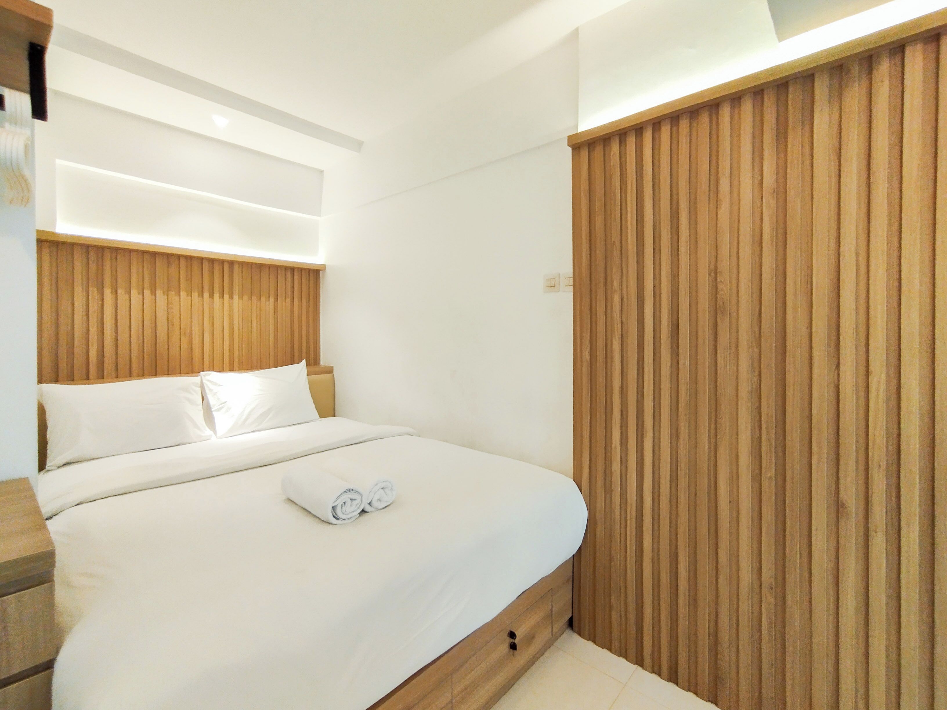 A modern bedroom with a wooden headboard, a neatly made bed with white linens, and a wooden panel wall.
