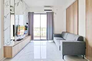 A modern living room with a flat-screen TV, a grey sofa, and a marble-patterned cabinet. - Comfort Living 2Br At Sky House Bsd Apartment (Pagedangan)