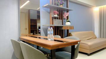 A modern living room with a wooden dining table, two chairs, a beige sofa, and a built-in shelving unit with decorative items.