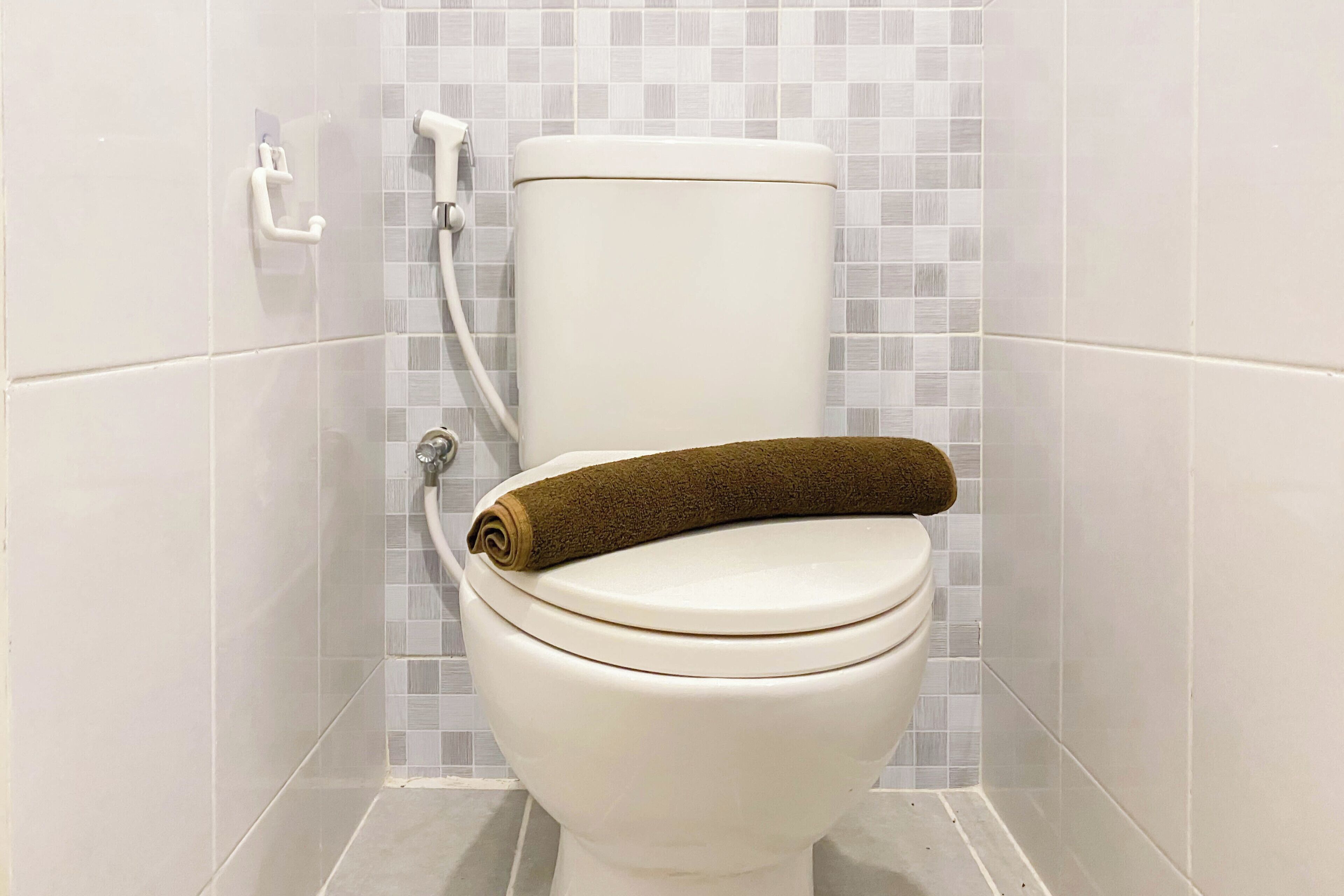A toilet with a brown towel on the seat, white tiles on the walls, and a white toilet tank.