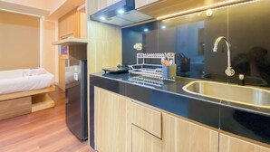 A compact kitchen with a black countertop, wooden cabinets, a stainless steel sink, and a built-in oven. - Good And Simply Studio Tokyo Riverside Pik 2 Apartment (Teluknaga)