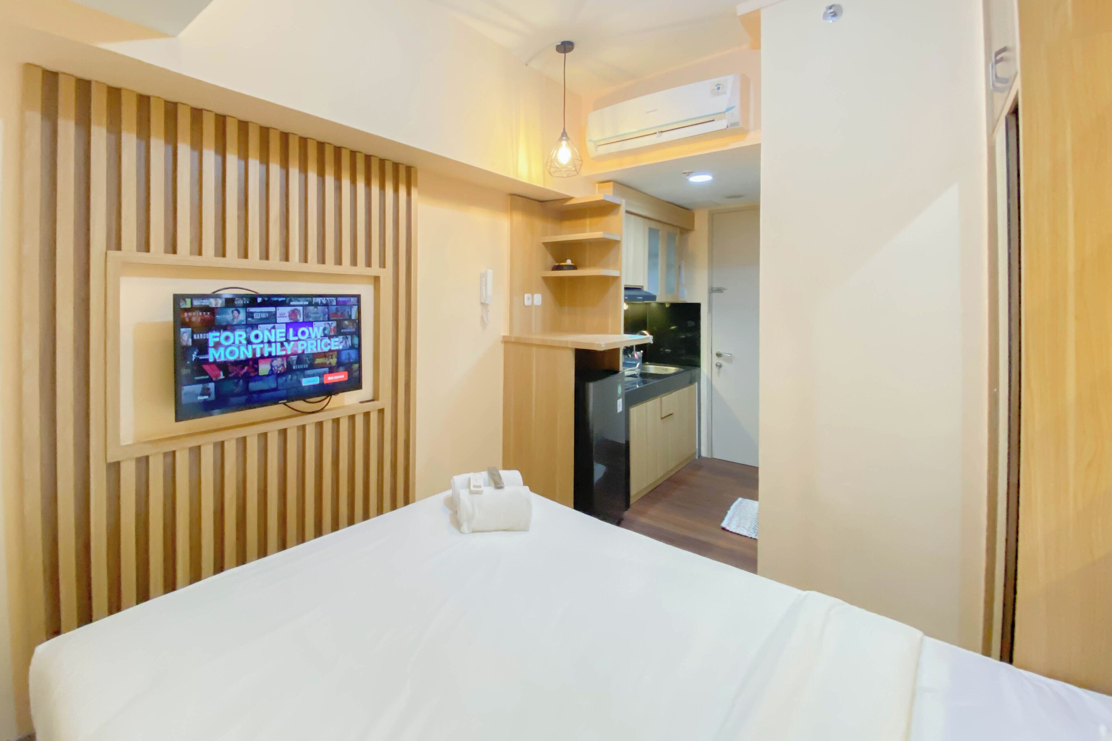Ein Hotelzimmer mit Bett, einem an der Wand befestigten Fernseher, einer kleinen Küchenzeile und einem Holzschrank.