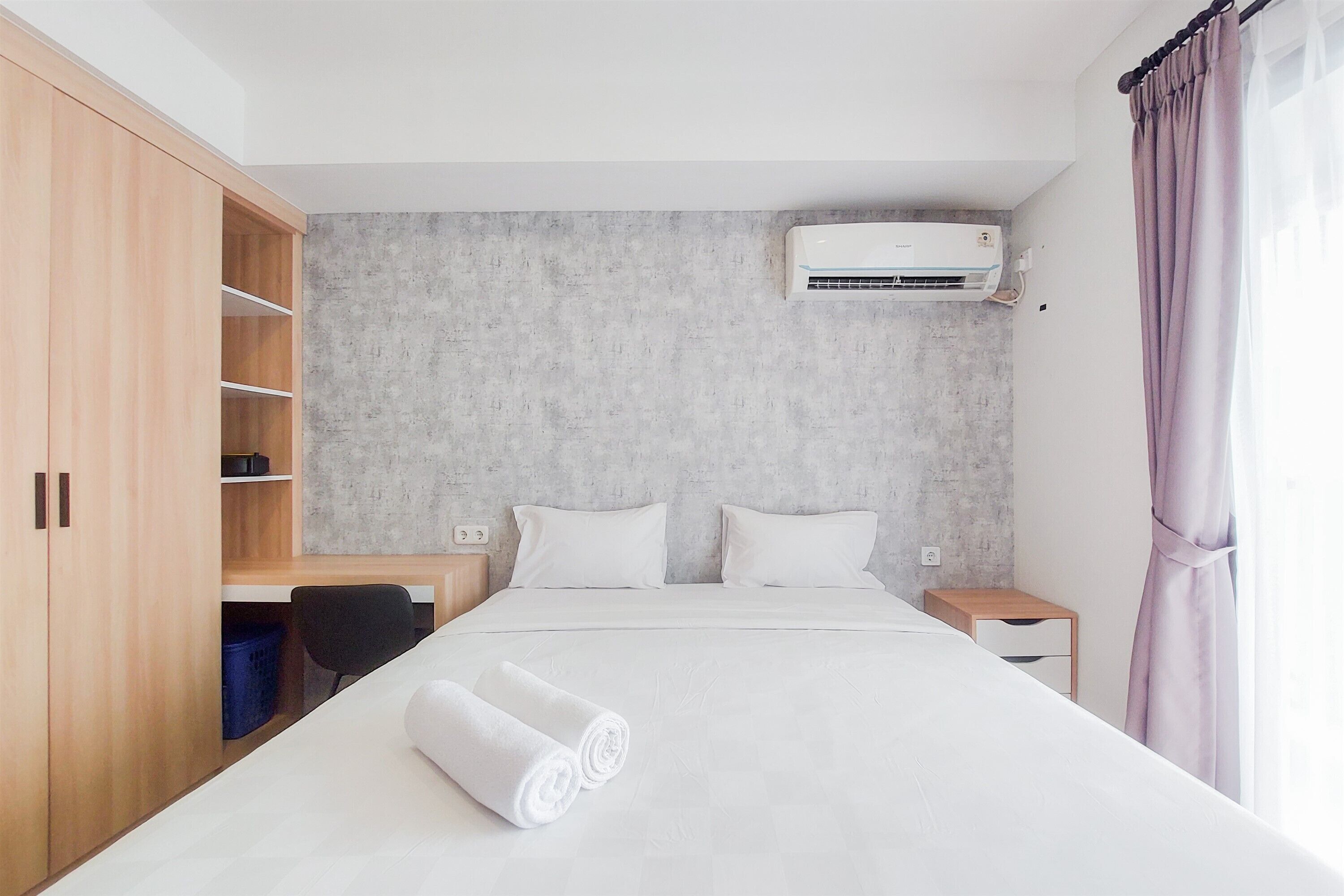 Hotellihuone, jossa on suuri sänky, työpöytä, tuoli, vaatekaappi, pieni yöpöytä ja ilmastointilaite.