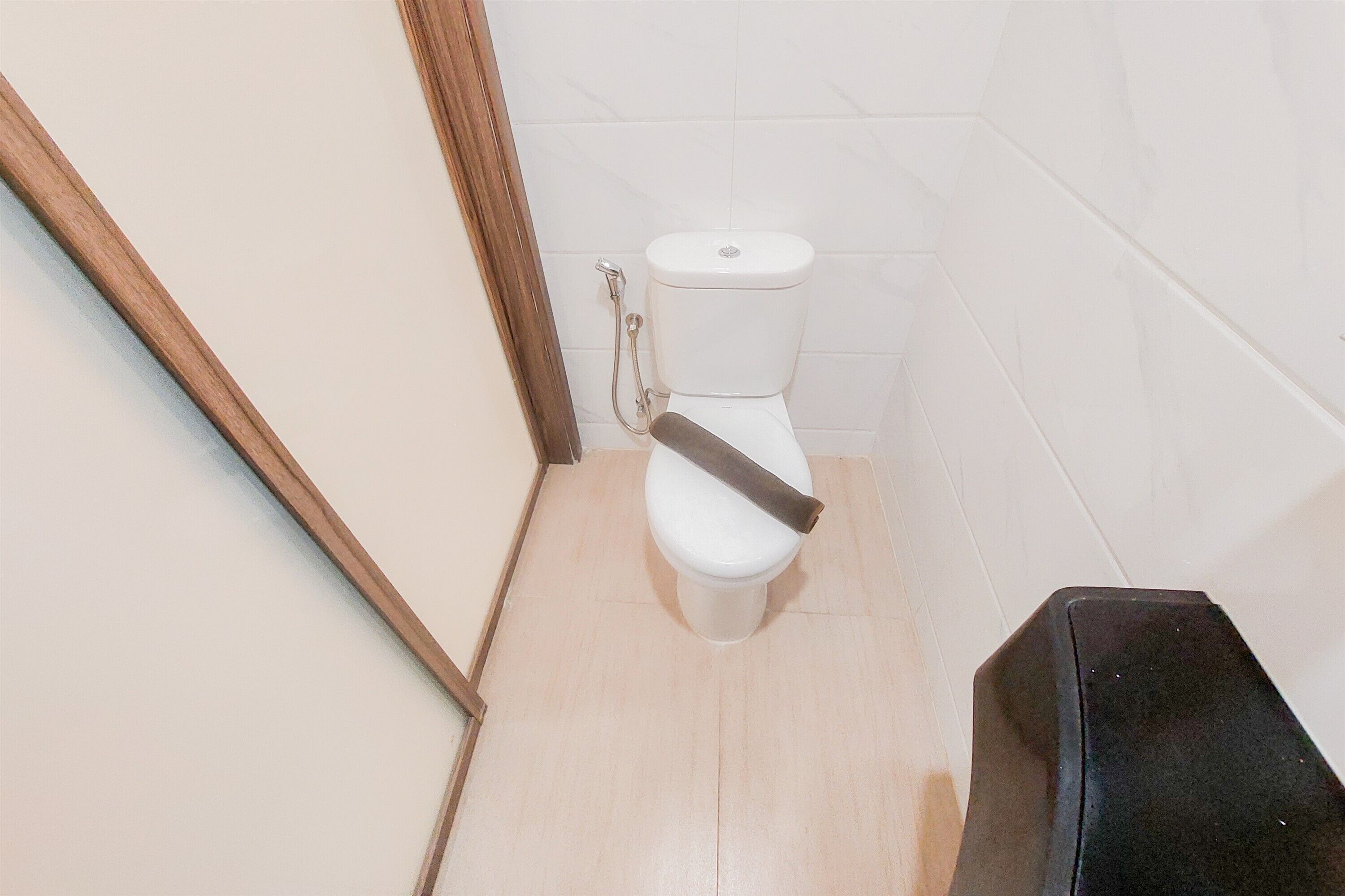 Un bagno con il water, una cornice di legno a sinistra e un cestino nero a destra.