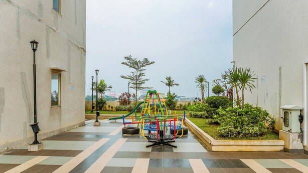 A playground with a climbing structure and a slide, surrounded by a paved area with a lamp post and greenery. - Good Deal And Homey Studio At Margonda Residence 4 Apartment (Depok)