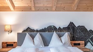 A bed with a grey headboard and white bedding, wooden nightstands, a wall-mounted lamp, and a mountain mural. - Glockner by Interhome (Heiligenblut)