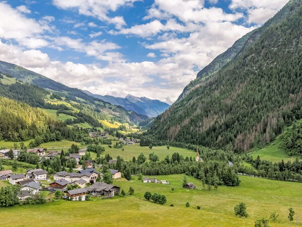 Un village rural niché dans une vallée, avec des maisons et une église, entouré de montagnes et de verdure.