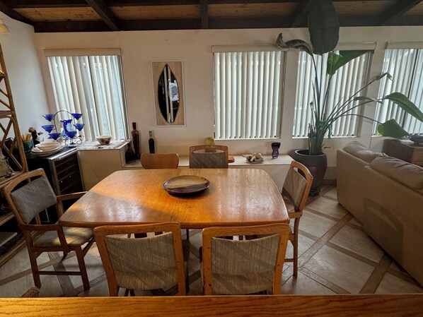 A dining area with a wooden table, four chairs, a sofa, and a large potted plant.