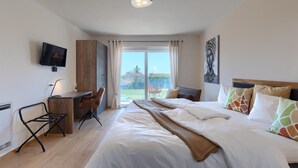 Una habitación de hotel moderna con una cama, un escritorio, una silla, un televisor y un ventanal con vistas al exterior.