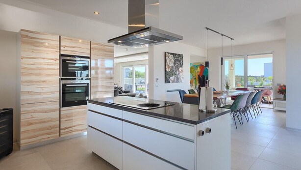 Una cocina moderna con hornos integrados, una isla central y un amplio ventanal con vistas a un patio.