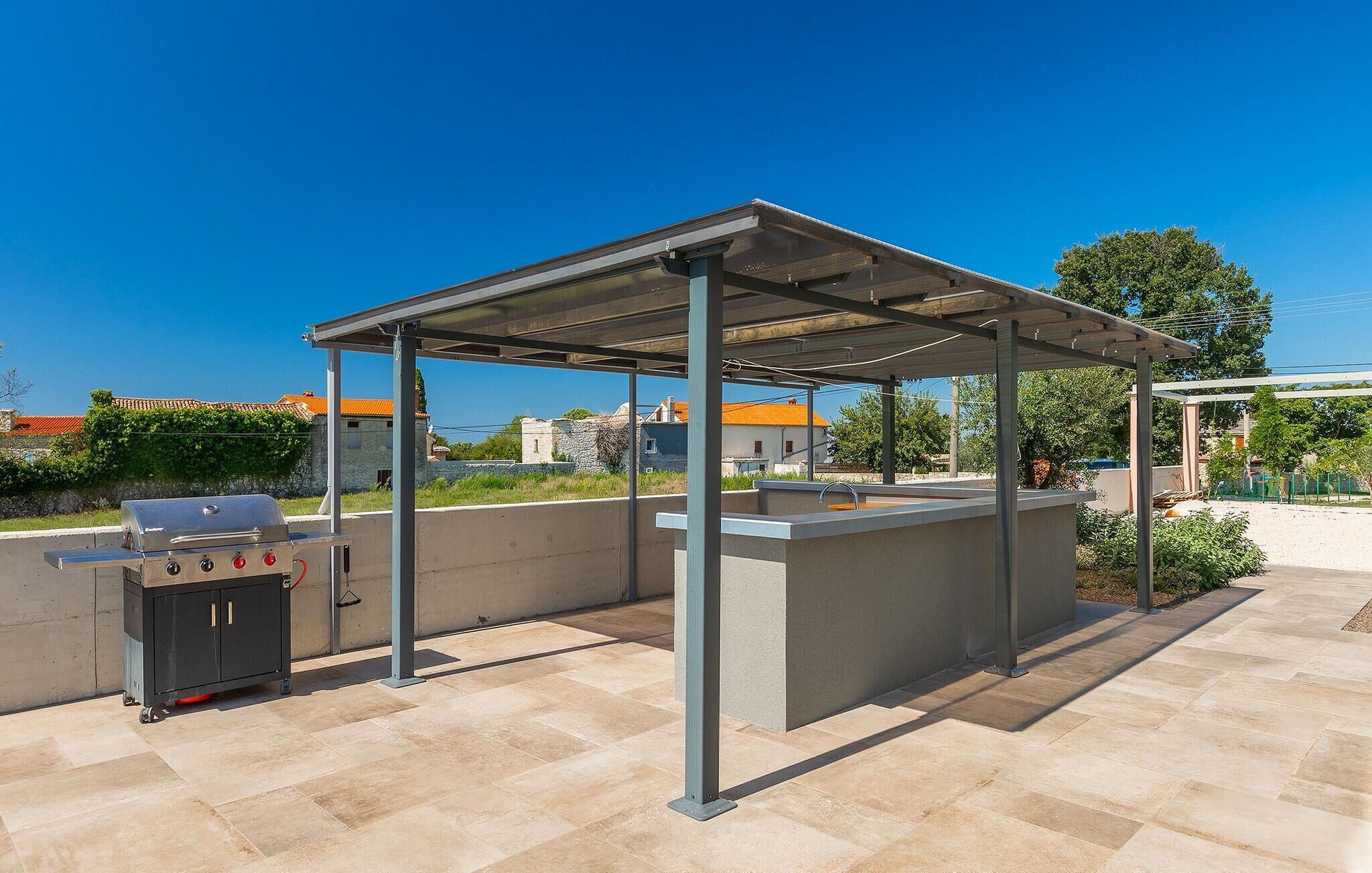 Een terras buiten met een barbecue, een overdekte zithoek en een stenen muur.