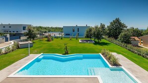 Una piscina con vistas a un césped cuidado, una zona de juegos infantiles y un edificio moderno al fondo.