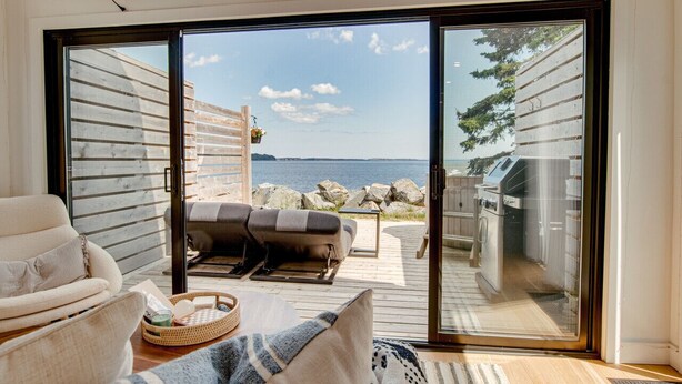 Una sala de estar moderna con un gran ventanal corredizo que da a una terraza con vista a un cuerpo de agua.