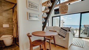 Un interior moderno con una mesa de comedor y sillas de madera, un sofá con vistas y una escalera que lleva a un balcón.