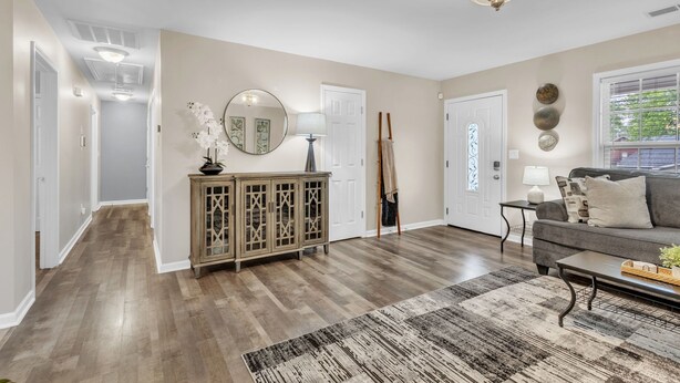 Een ruime woonkamer met houten vloeren, een grote bank, een salontafel en een open haard.