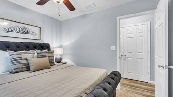 A bedroom with a bed, a ceiling fan, a door, and a framed artwork on the wall.
